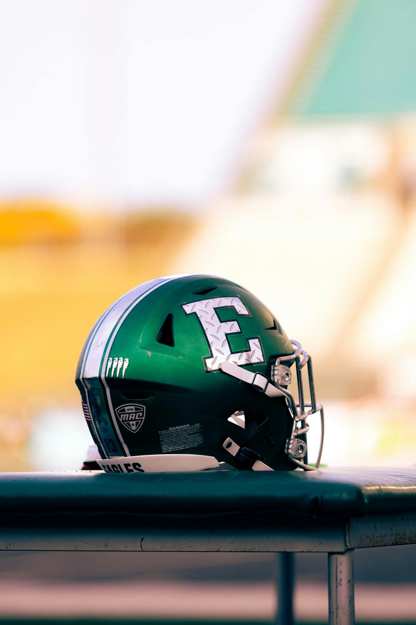 A green football helmet featuring a grey stylized block E sits perched atop an equipment table. 