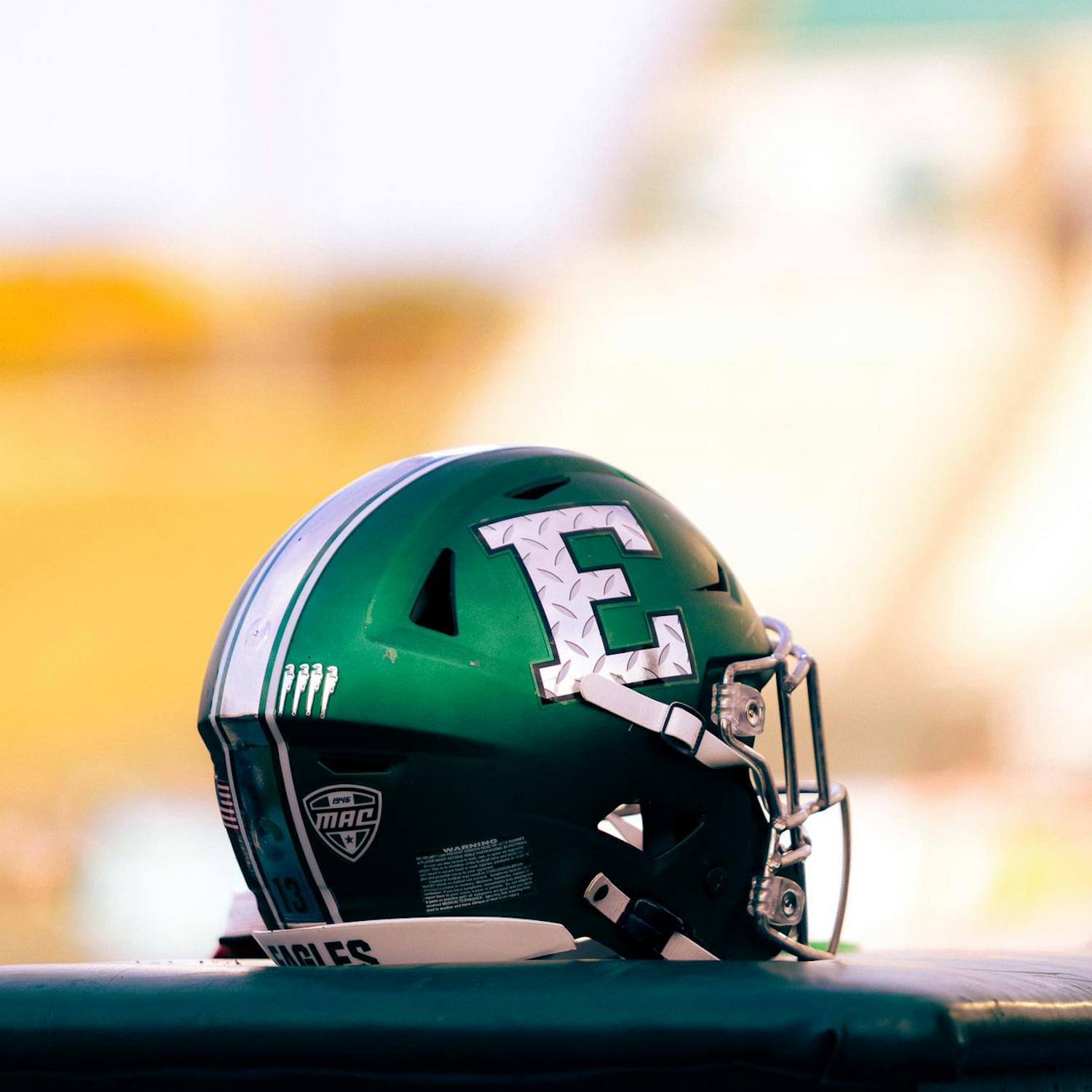 A green football helmet featuring a grey stylized block E sits perched atop an equipment table.
