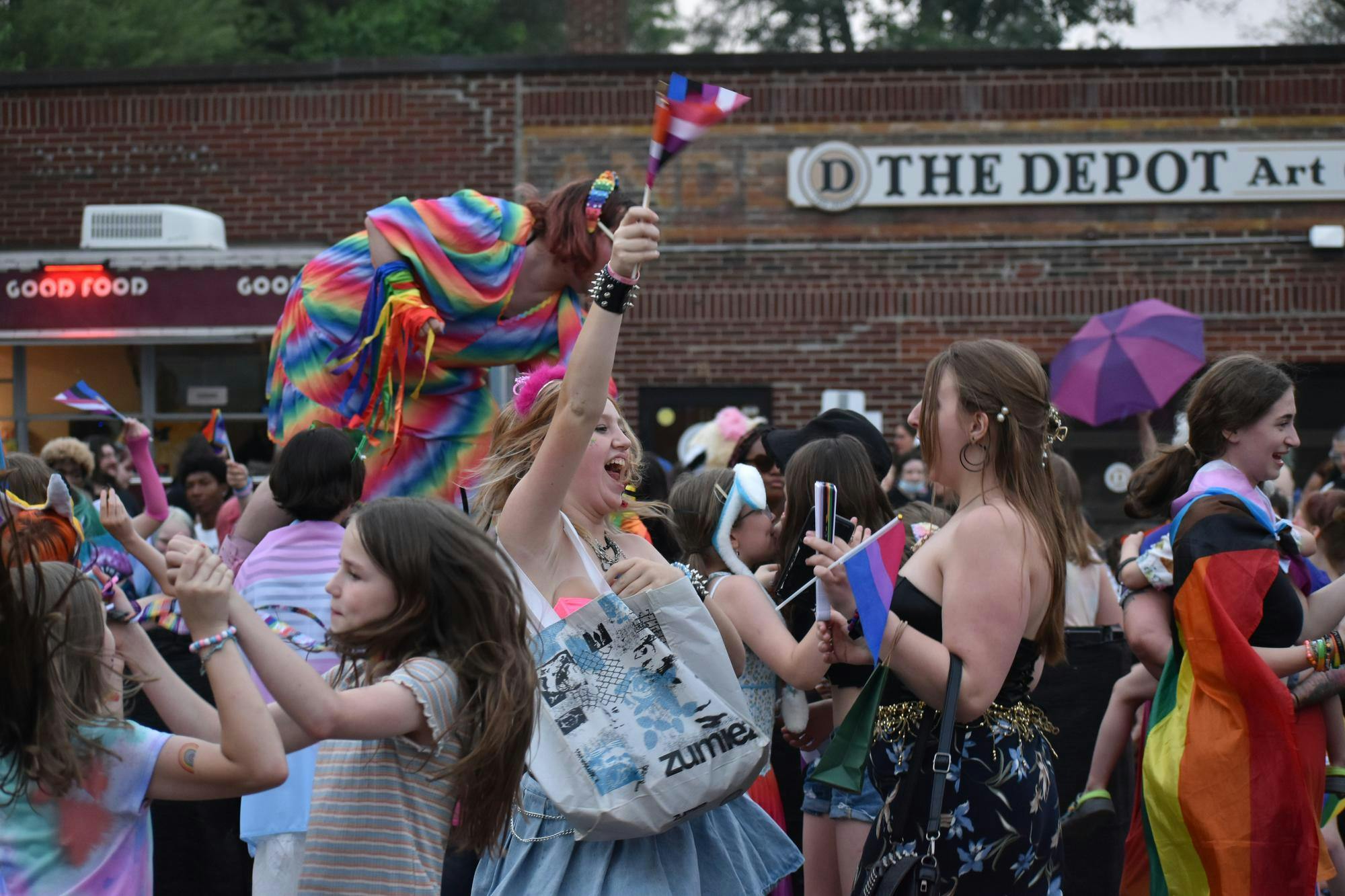 Street full of people close together and dancing. Many attendees wear colorful makeup and outfits.