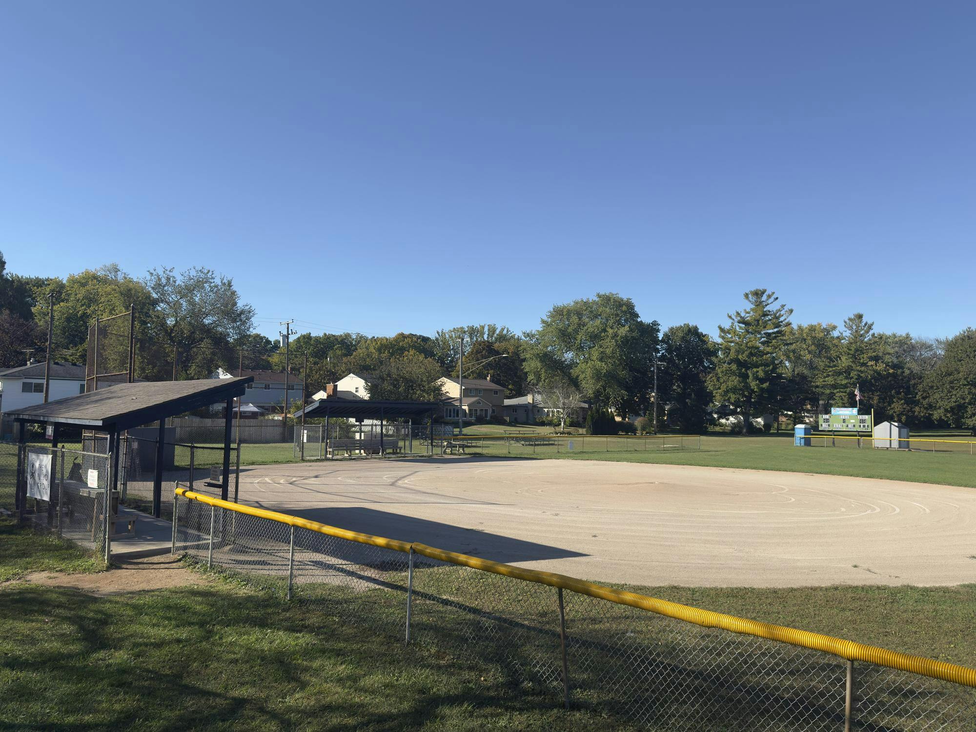 A baseball field surrounded by fencing, grass, and dugout areas for the team.