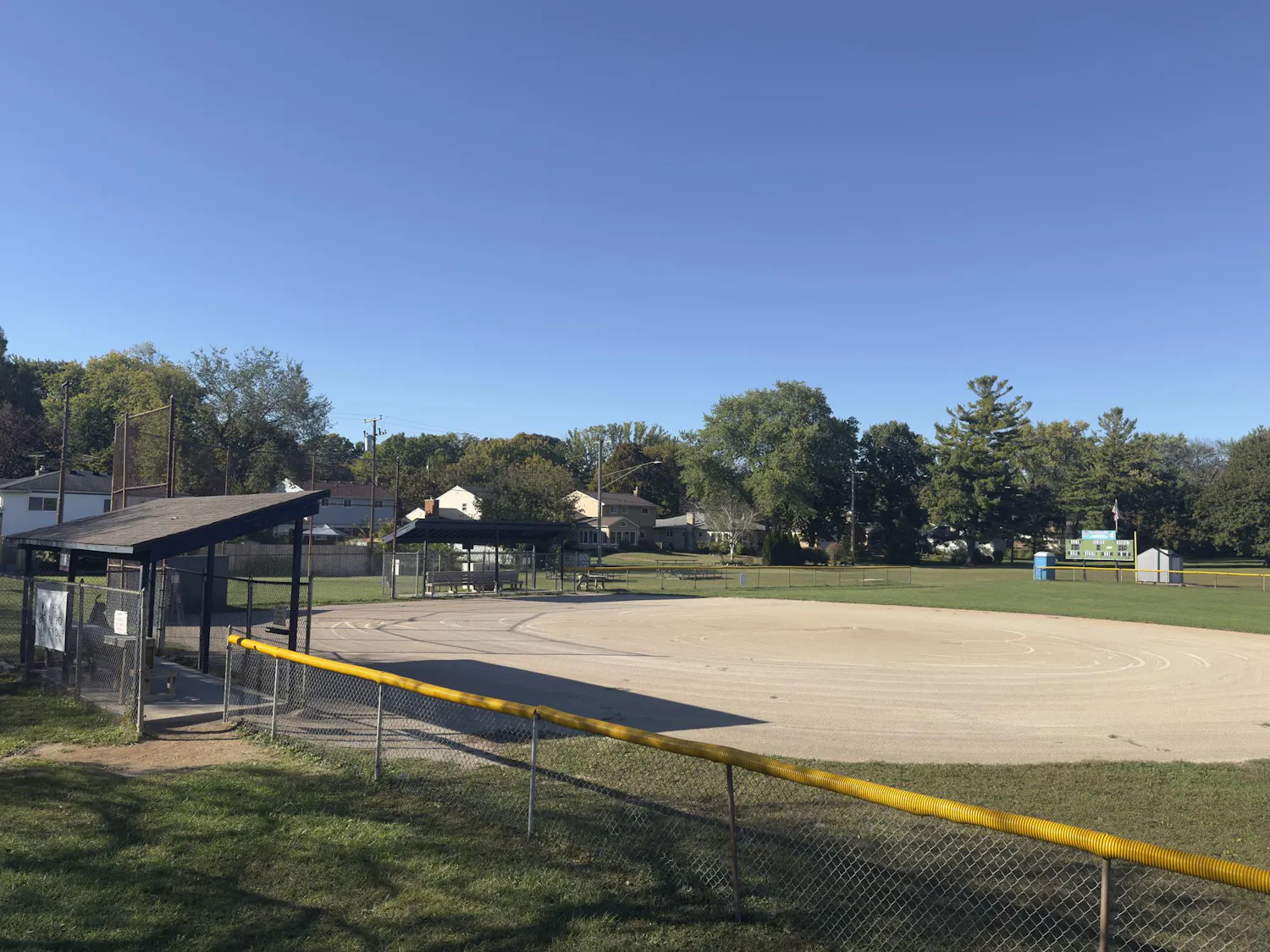 A baseball field surrounded by fencing, grass, and dugout areas for the team.