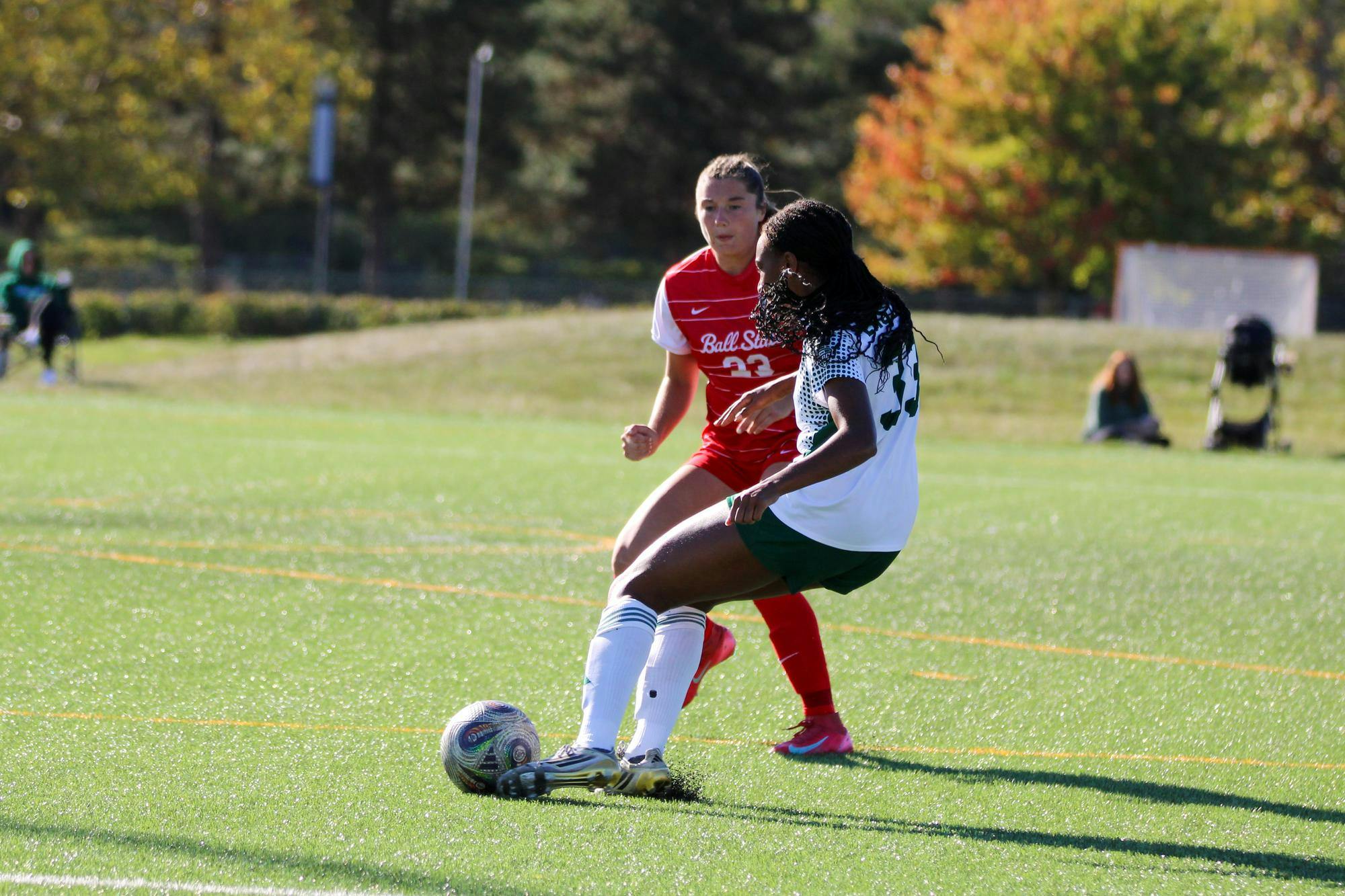 EMU player, in a white jersey, kicking the soccer ball in front of a Ball State player, in a red jersey. 