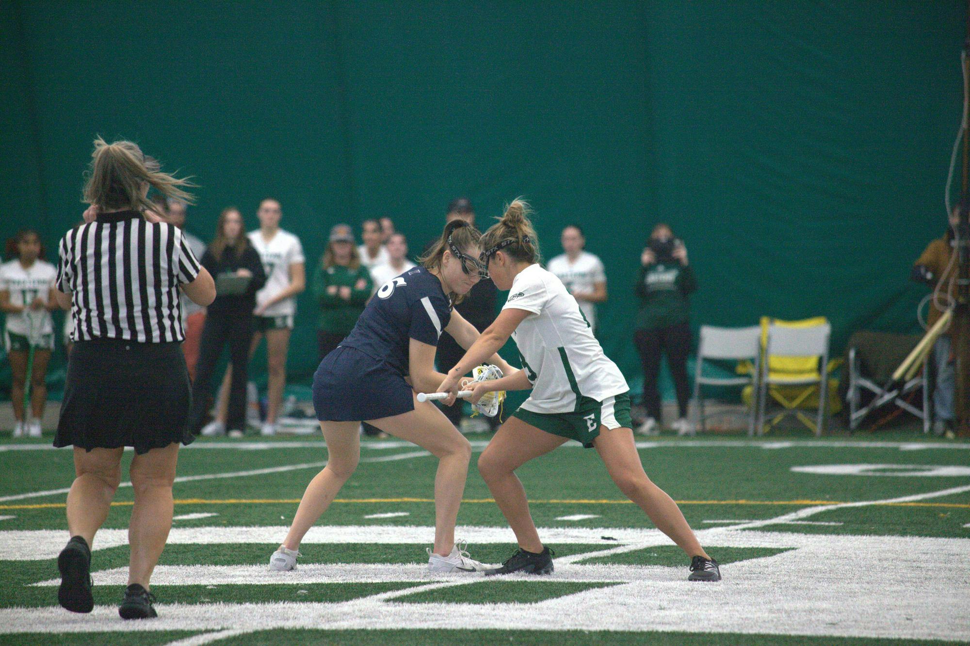 Women's lacrosse of opposing teams faceoff in the middle of the field before a play.