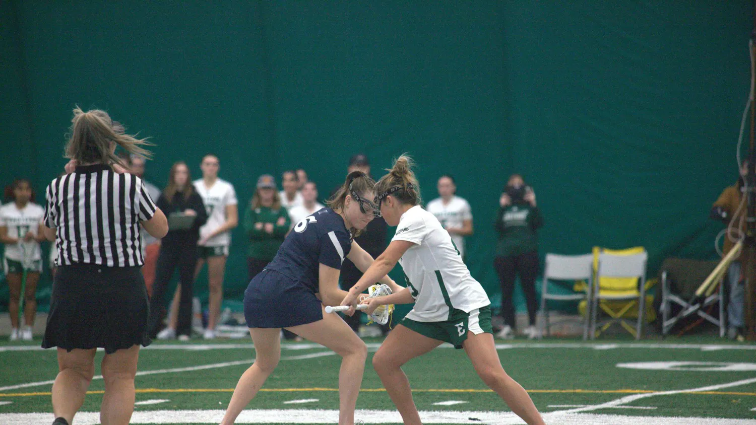 Women's lacrosse of opposing teams faceoff in the middle of the field before a play.
