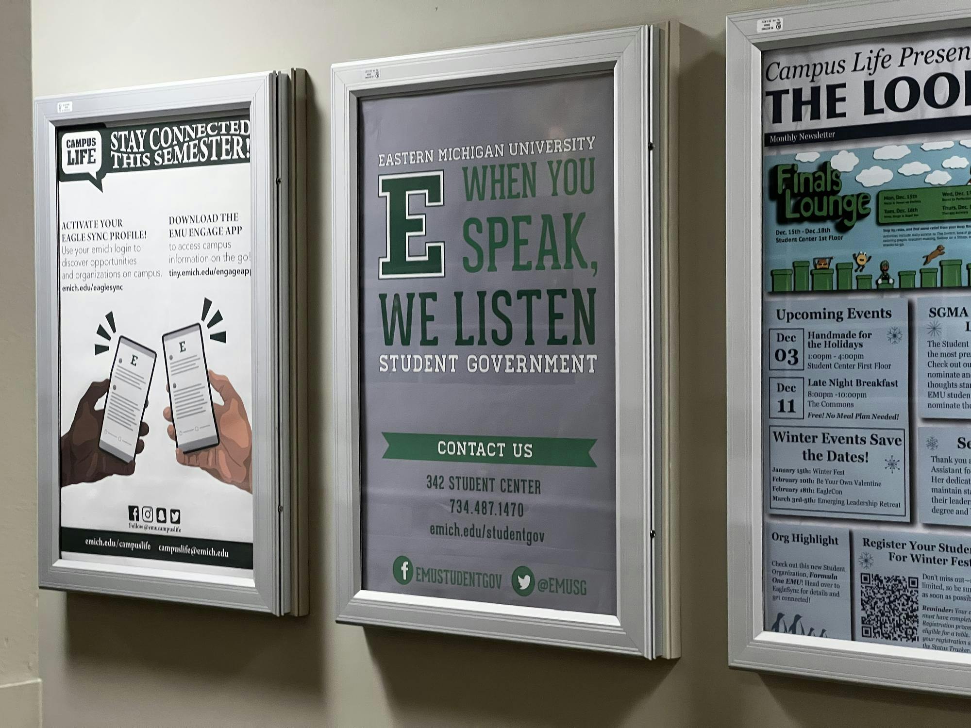 A framed poster on the wall reads, "WHEN YOU SPEAK, WE LISTEN," and has contact information for EMU Student Government at room 342 of the Student Center. The phone number is 734-487-1470 and the website is emich.edu/studentgov. EMUSTUDENTGOV on Facebook and @EMUSG on Twitter.