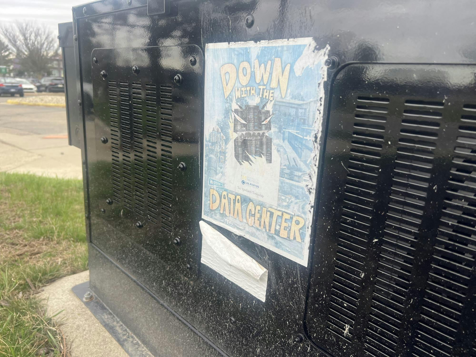 A weather-damaged flyer stuck to an electrical transformer on EMU's campus depicts a data center monster surrounded by the words "down with the data center."