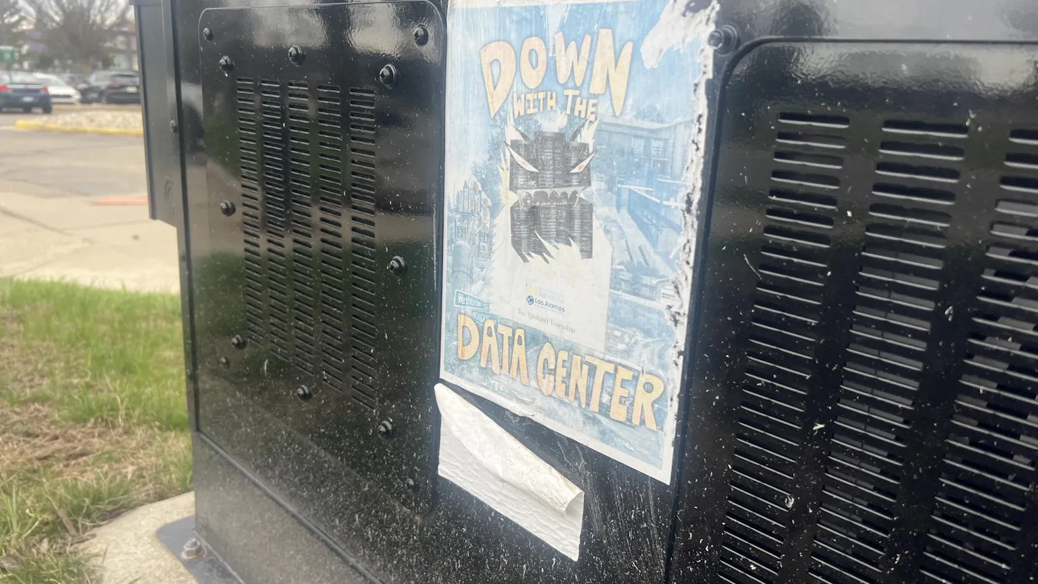 A weather-damaged flyer stuck to an electrical transformer on EMU's campus depicts a data center monster surrounded by the words "down with the data center."