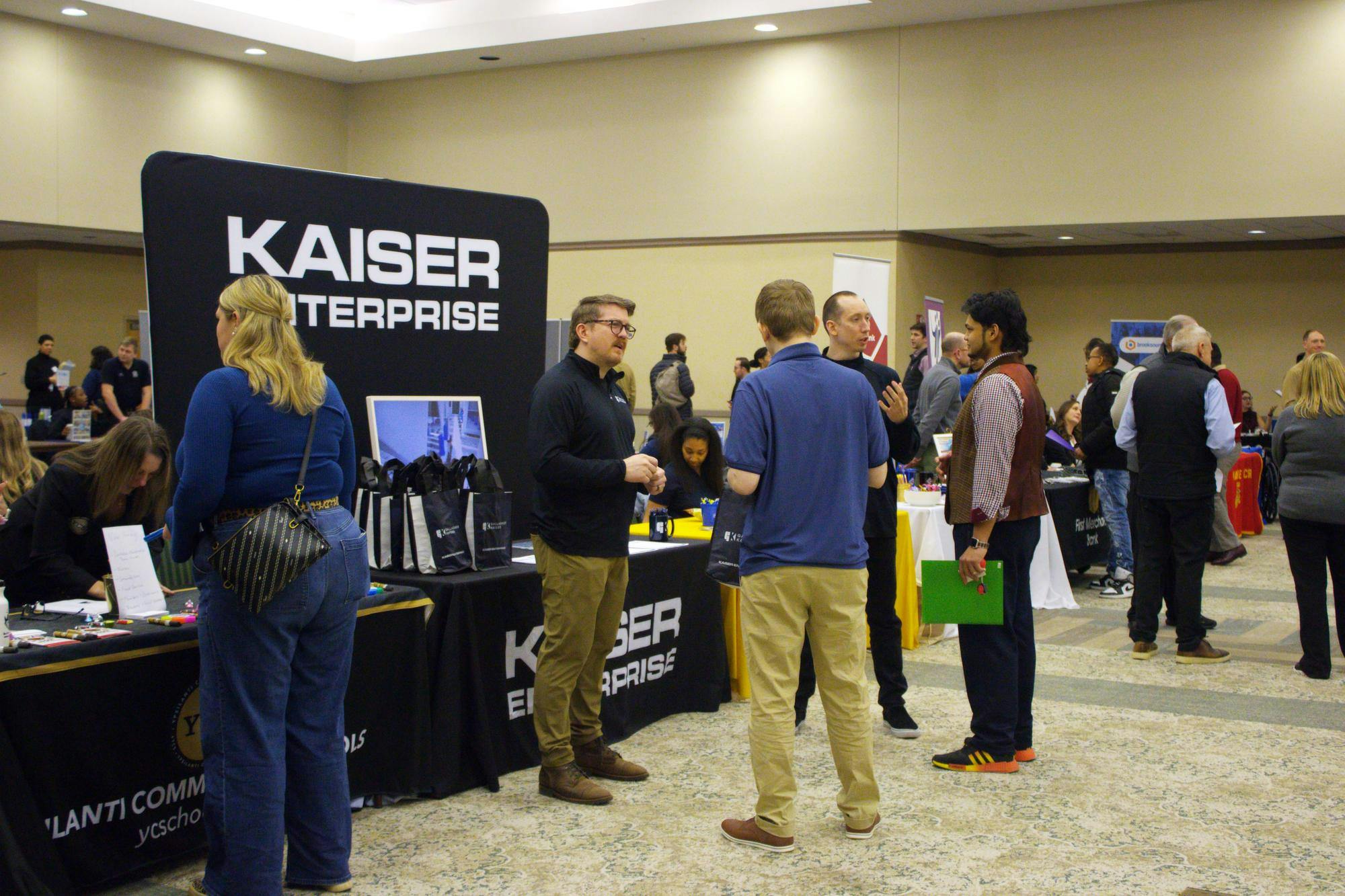 EMU students gather around a table with a big black display sign that reads 'Kaiser Enterprise' in white letters.