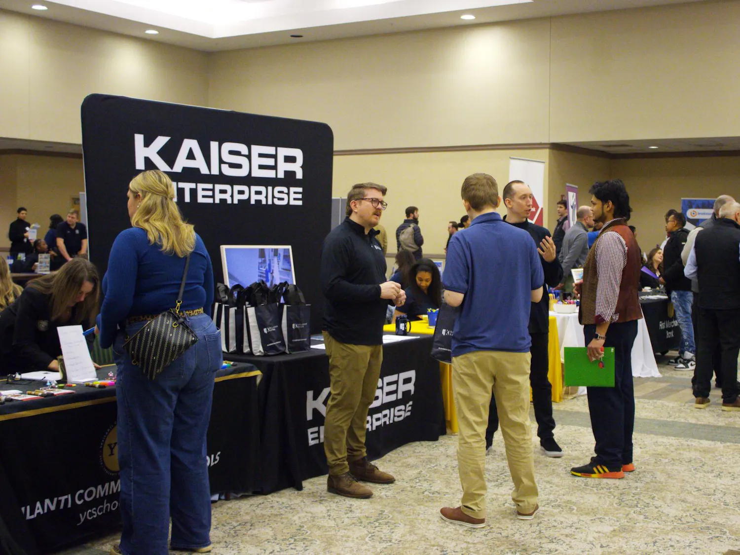 EMU students gather around a table with a big black display sign that reads 'Kaiser Enterprise' in white letters.
