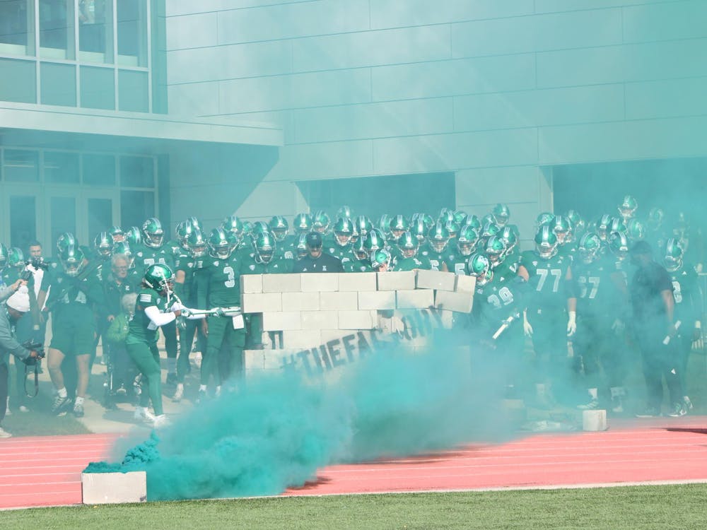 The Eastern Michigan University football team prepares to enter the field inside 'The Factory' amidst the green smoke as they break down the wall barriers with hammers. 
