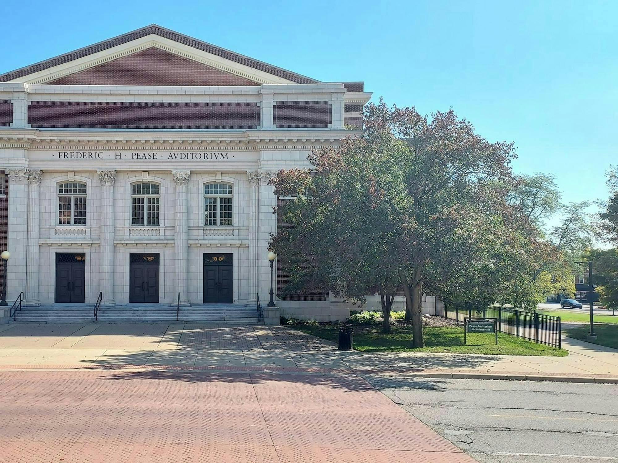 A building with white column-style architecture is located next to greenery and trees and contains the words "Frederic H. Pease Auditorium."