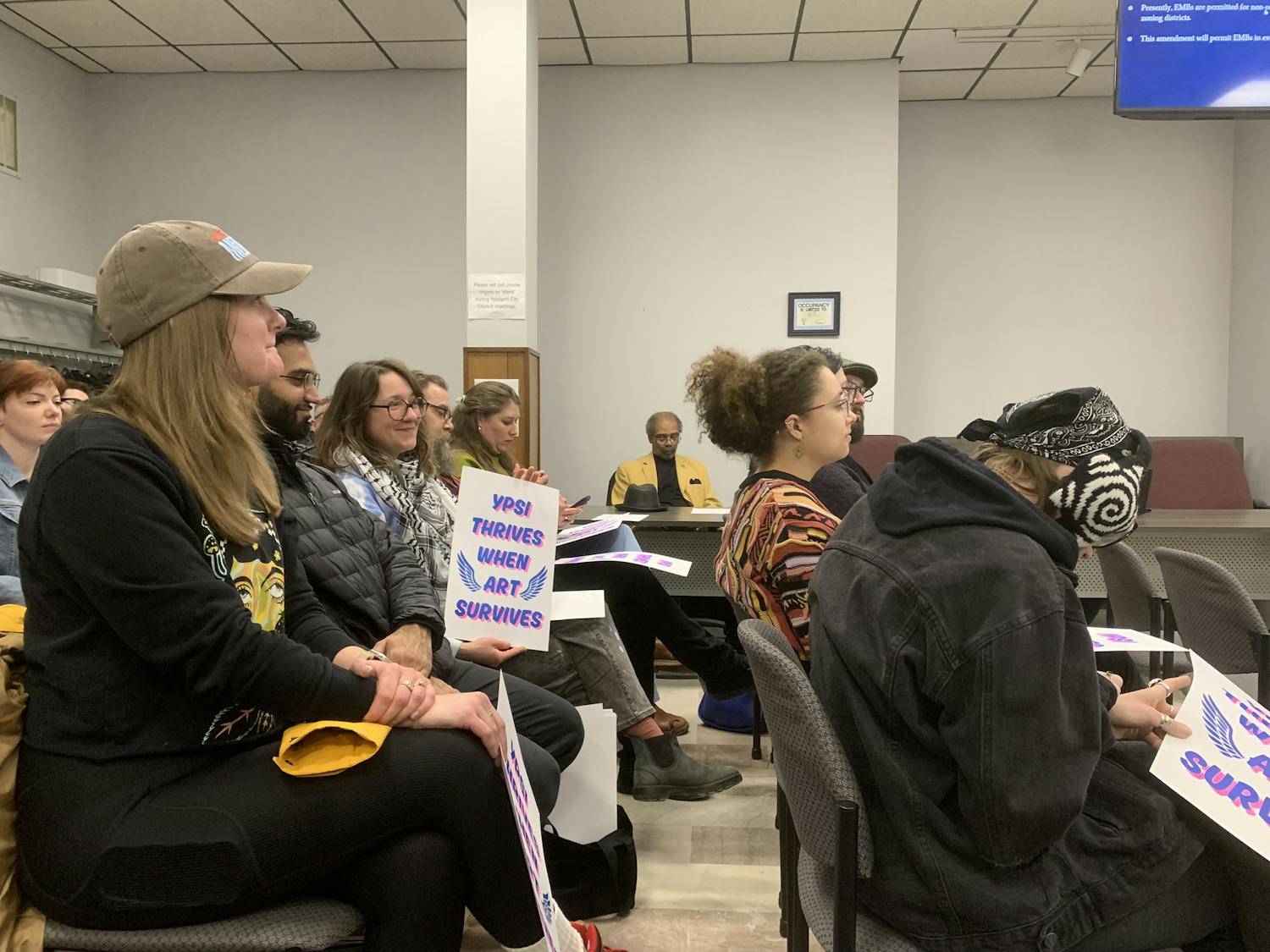 A dozen or so people sit in the audience of Ypsilanti City Hall, holding signs that say "Ypsi thrives when art survives."