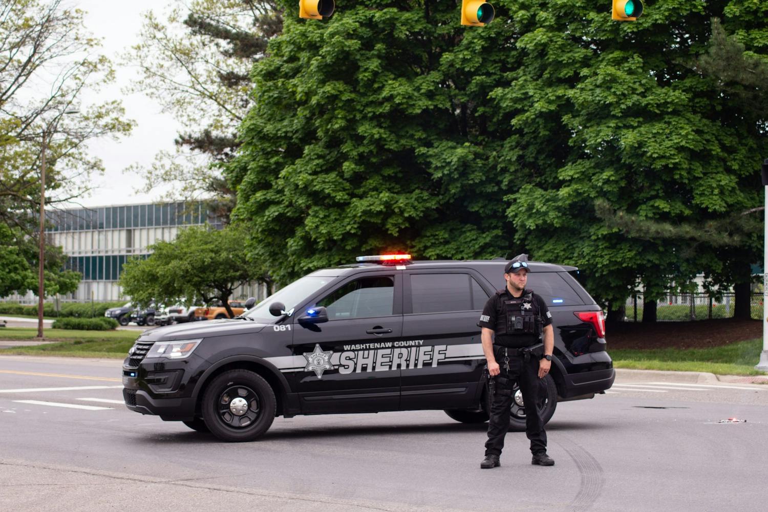 An officer for the Washtenaw County Sheriff's Department stands outside his vehicle parked on Textile Rd. in Ypsilanti