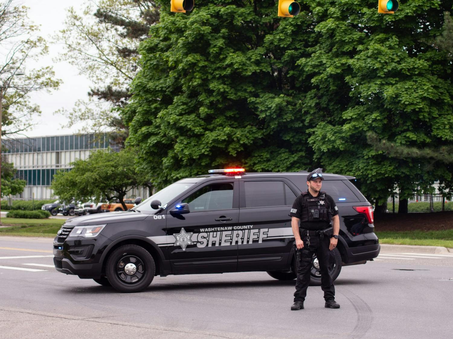 An officer for the Washtenaw County Sheriff's Department stands outside his vehicle parked on Textile Rd. in Ypsilanti
