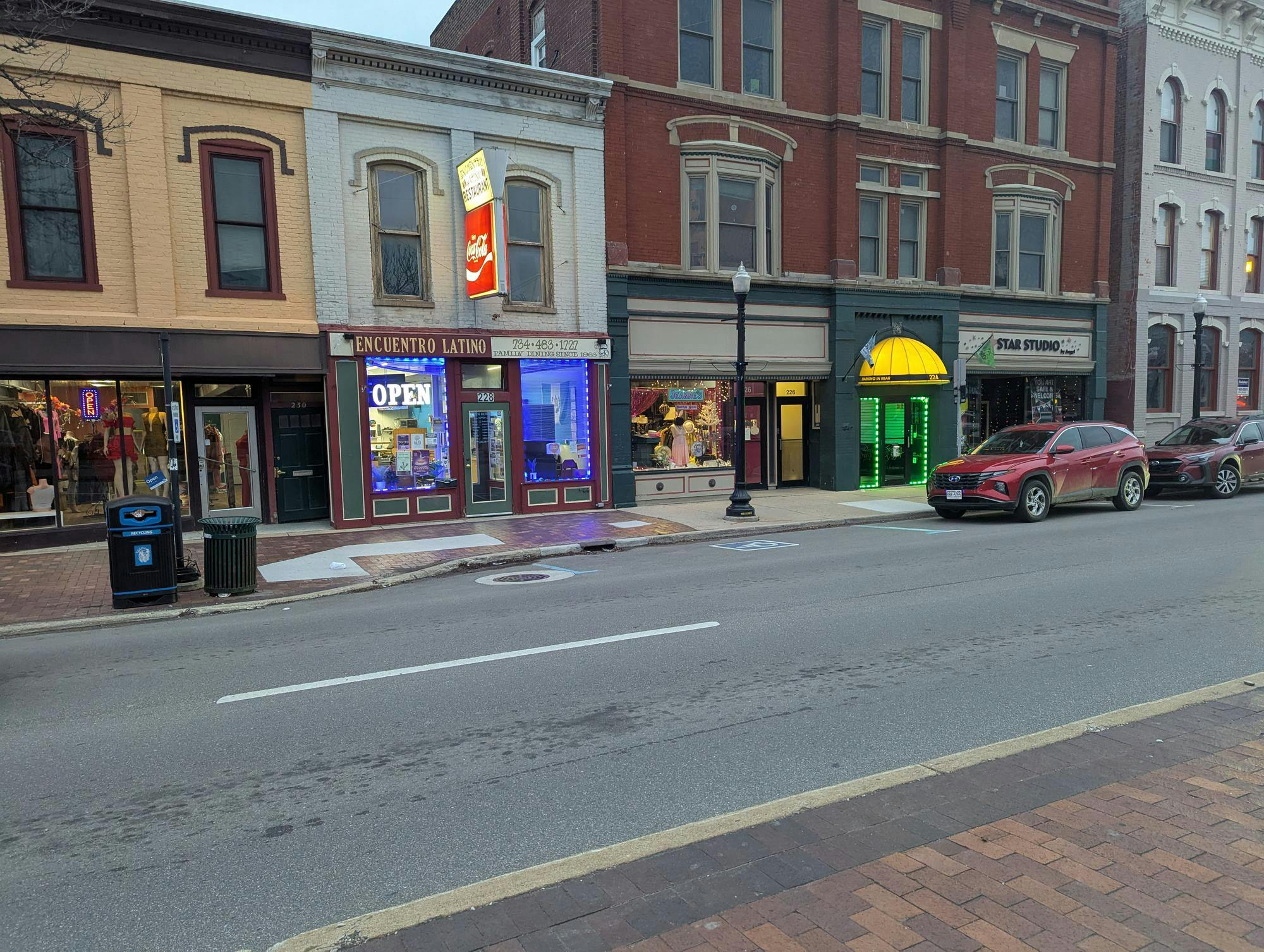 Downtown road with cars parked along sidewalks. Historic storefronts line the road.