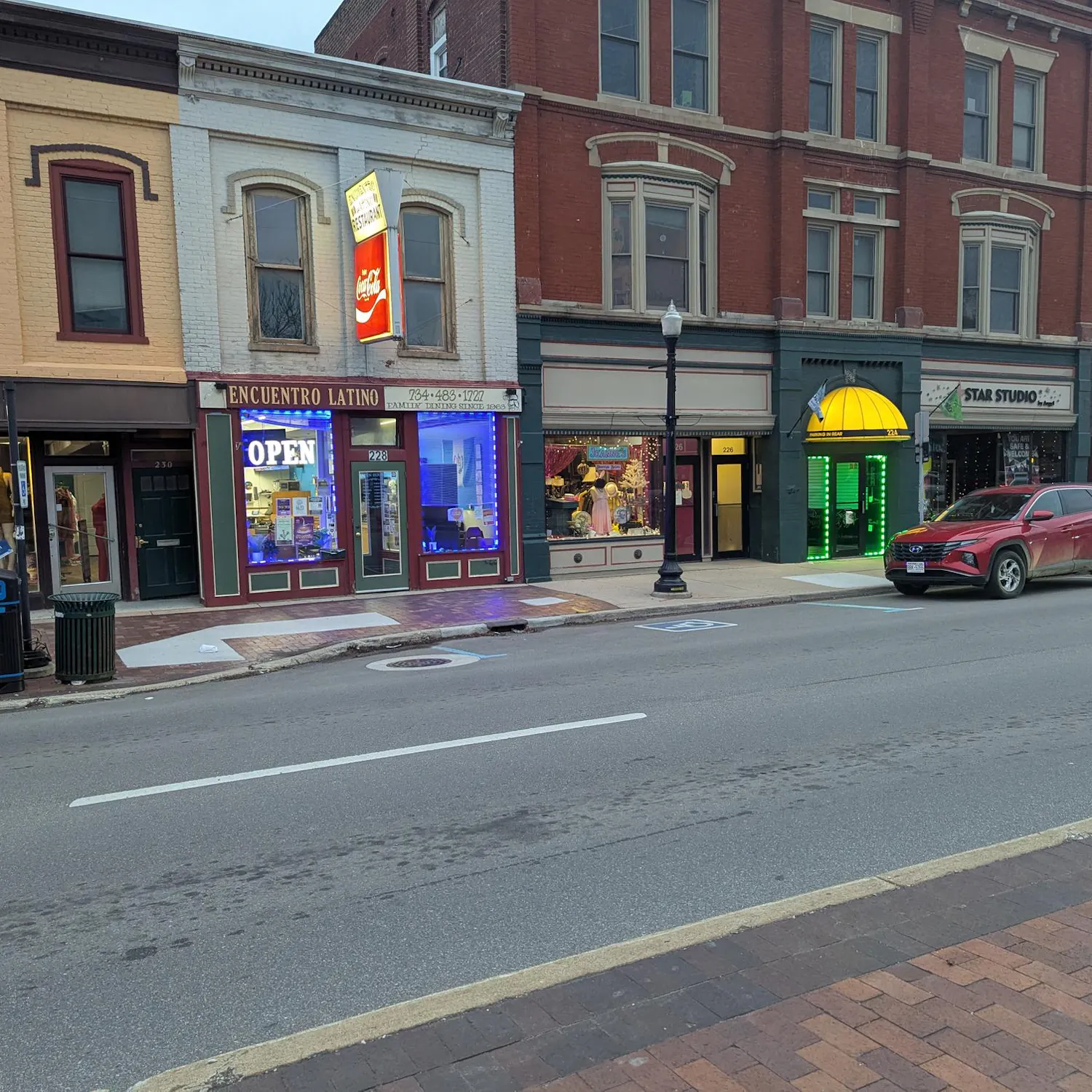 Downtown road with cars parked along sidewalks. Historic storefronts line the road.