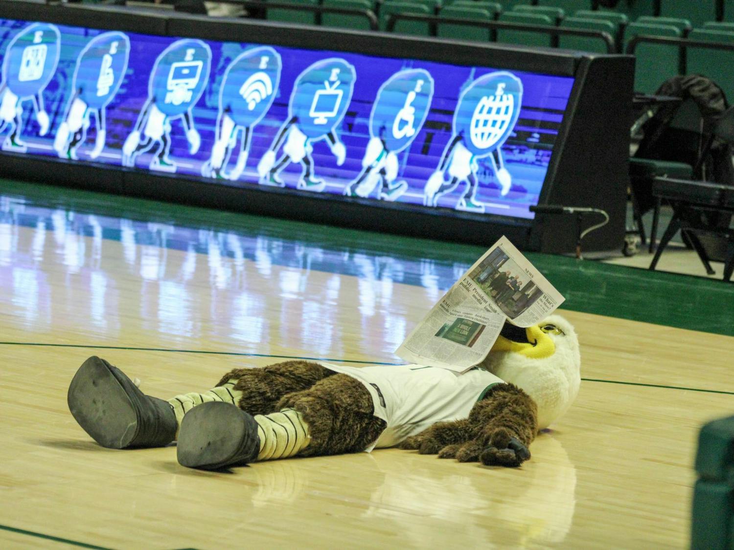 Swoop, EMU's mascot, is reading The Eastern Echo newspaper while lying on his back on the basketball court.