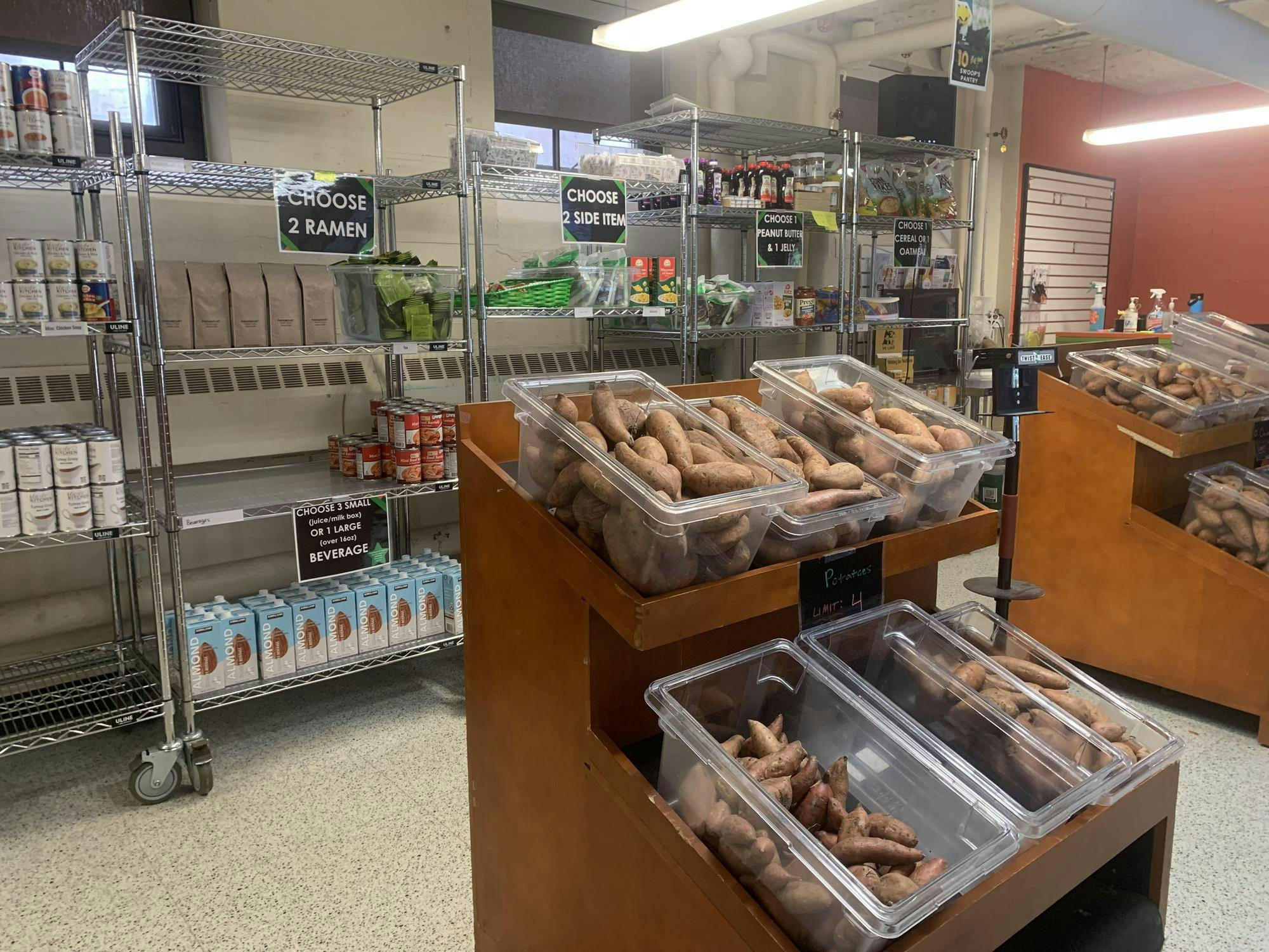 A shelf full of a variety of food items sits because a smaller shelf of vegetables inside of Swoop's Pantry. 