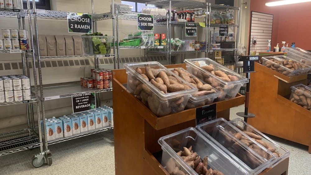 A shelf full of a variety of food items sits because a smaller shelf of vegetables inside of Swoop's Pantry.