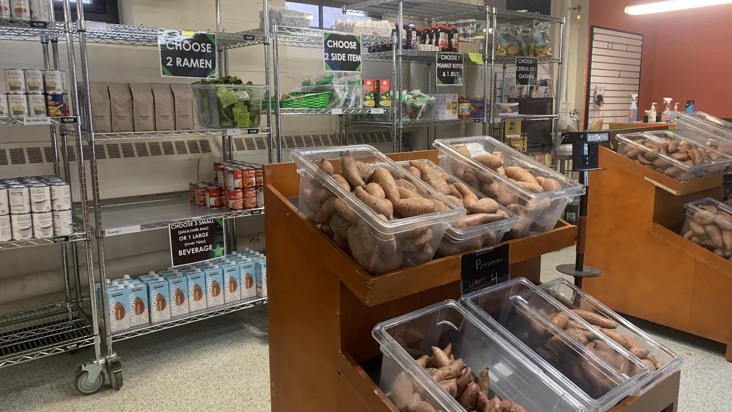 A shelf full of a variety of food items sits because a smaller shelf of vegetables inside of Swoop's Pantry.