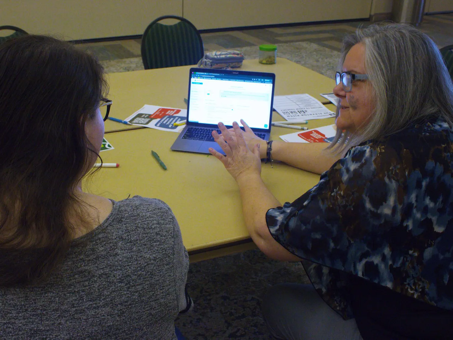 A student and an EMU faculty member sit facing a laptop that rests on a cluttered table.