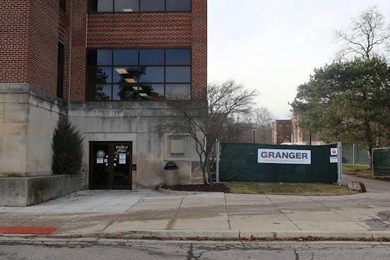 Green construction fences surround Pierce Hall, a gray cement and red brick building. A sign reading "Granger" is attached to the fence, representing the construction company.
