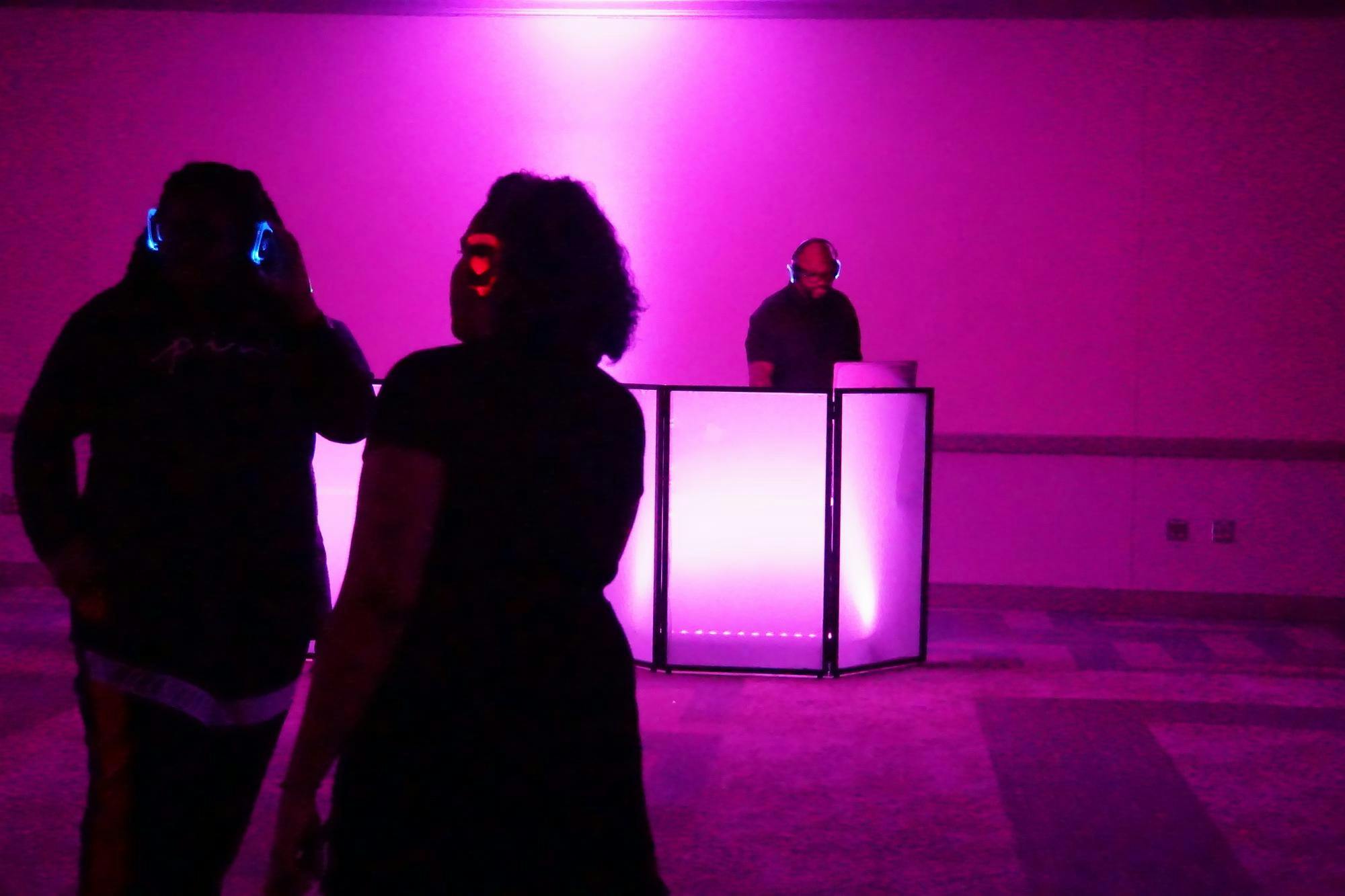 A view of two students dancing together with one of the DJs in the background.