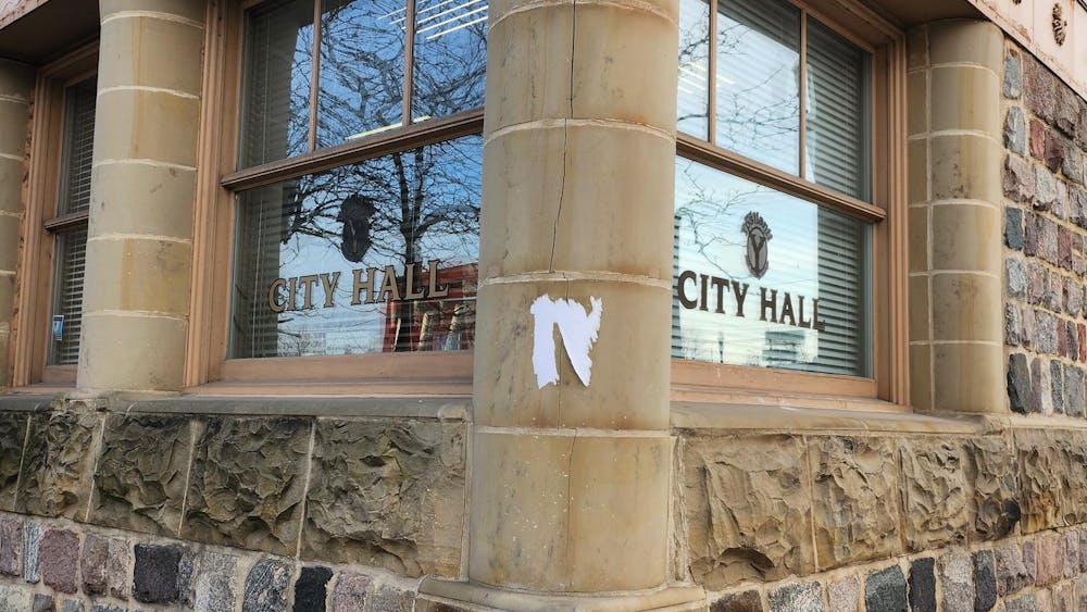 The corner of Ypsilanti City Hall building at 1 South Huron St. during daylight hours shows two windows a a 90-degree angle, and the stone foundation.