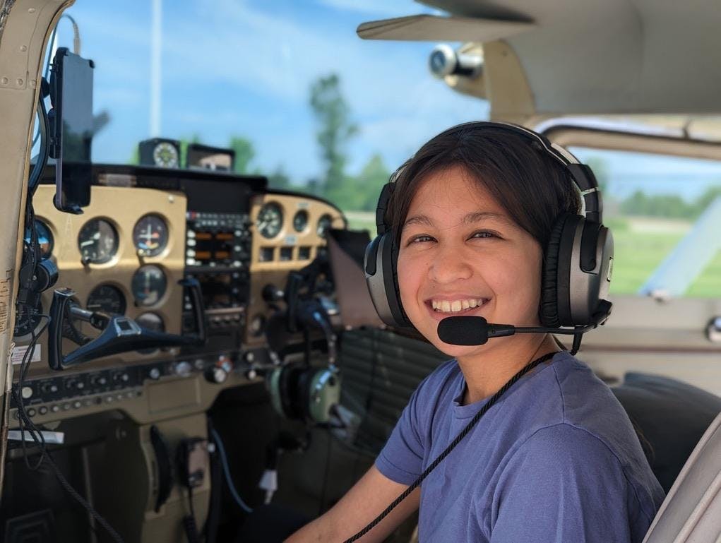 A girl in a plane smiles while wearing a headset.