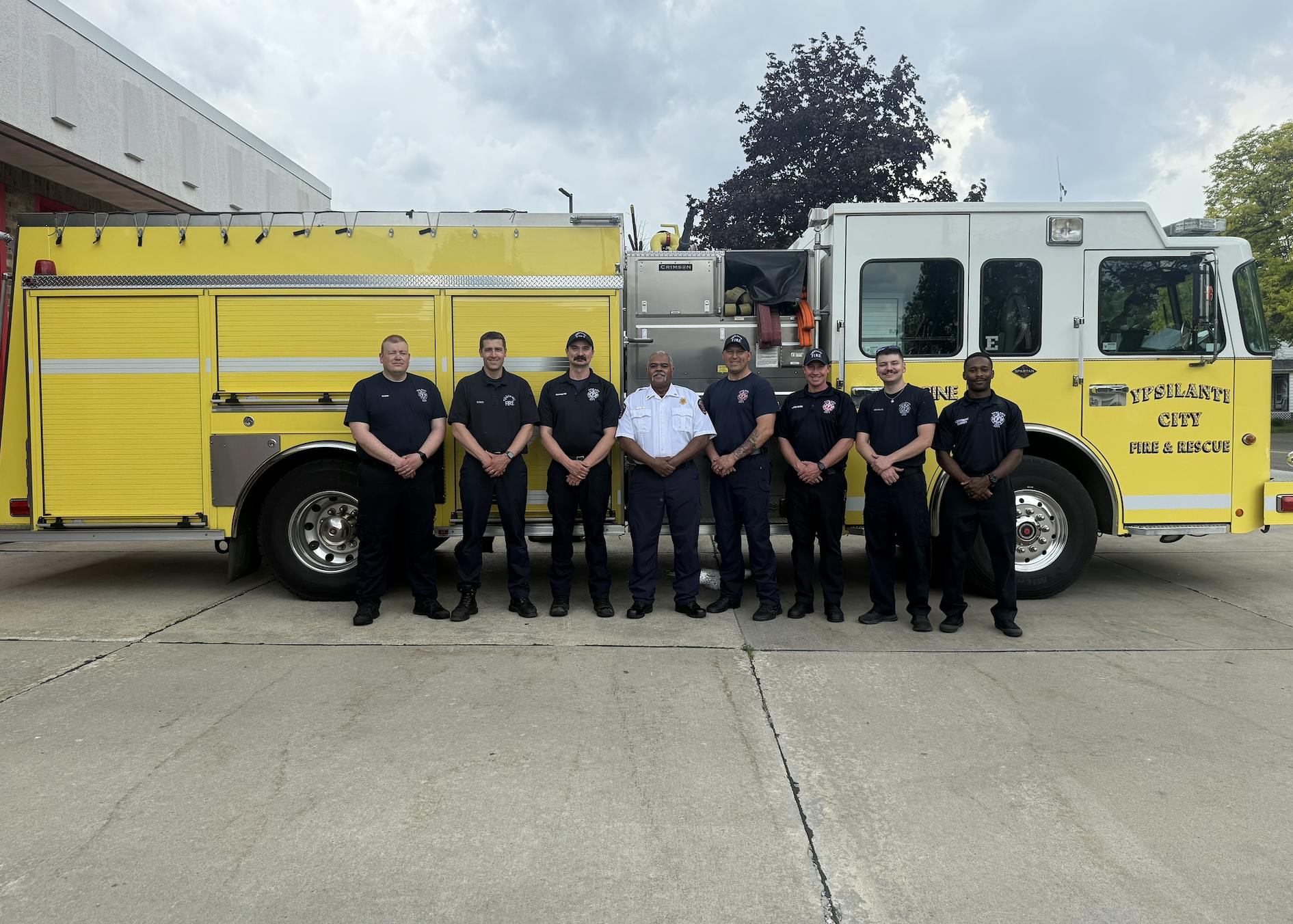 A yellow fire engine with a group of firefighters standing in front of it.