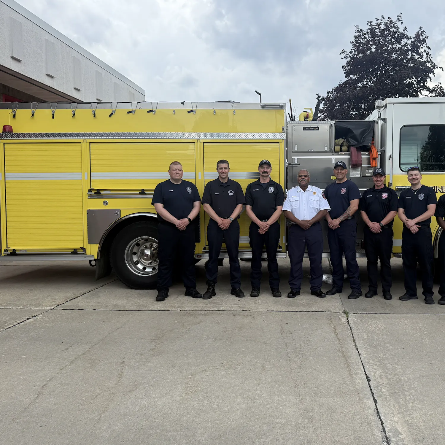 A yellow fire engine with a group of firefighters standing in front of it.