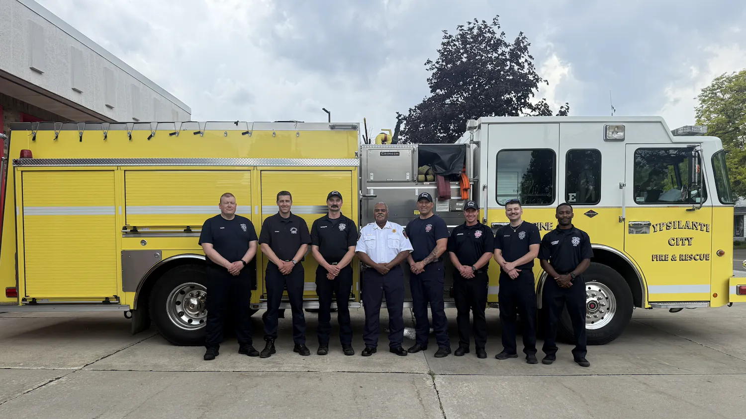 A yellow fire engine with a group of firefighters standing in front of it.
