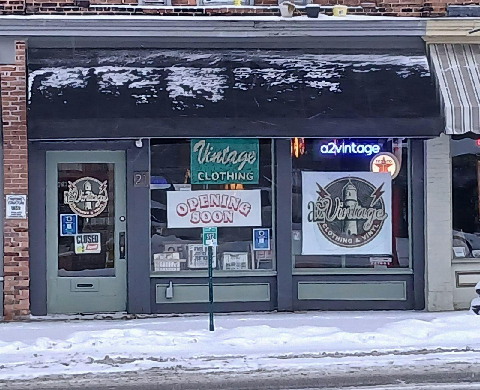 Storefront with green and black trim against a brick building. Multiple signs in the windows read "a2vintage," "Vintage Clothing," "Opening Soon" and more.