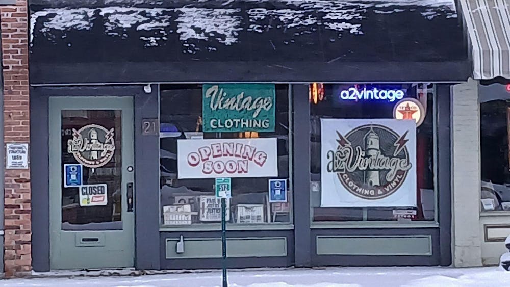 Storefront with green and black trim against a brick building. Multiple signs in the windows read "a2vintage," "Vintage Clothing," "Opening Soon" and more.