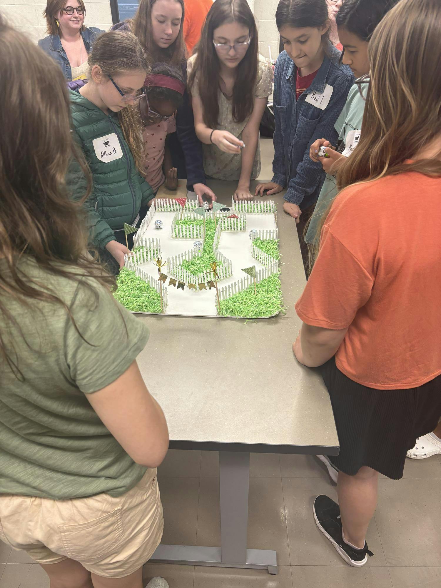 Several middle school girls from the Bits and Bytes camp gather around a maze they made and watch with keen attention to see whose Ozobot can finish the maze the fastest.