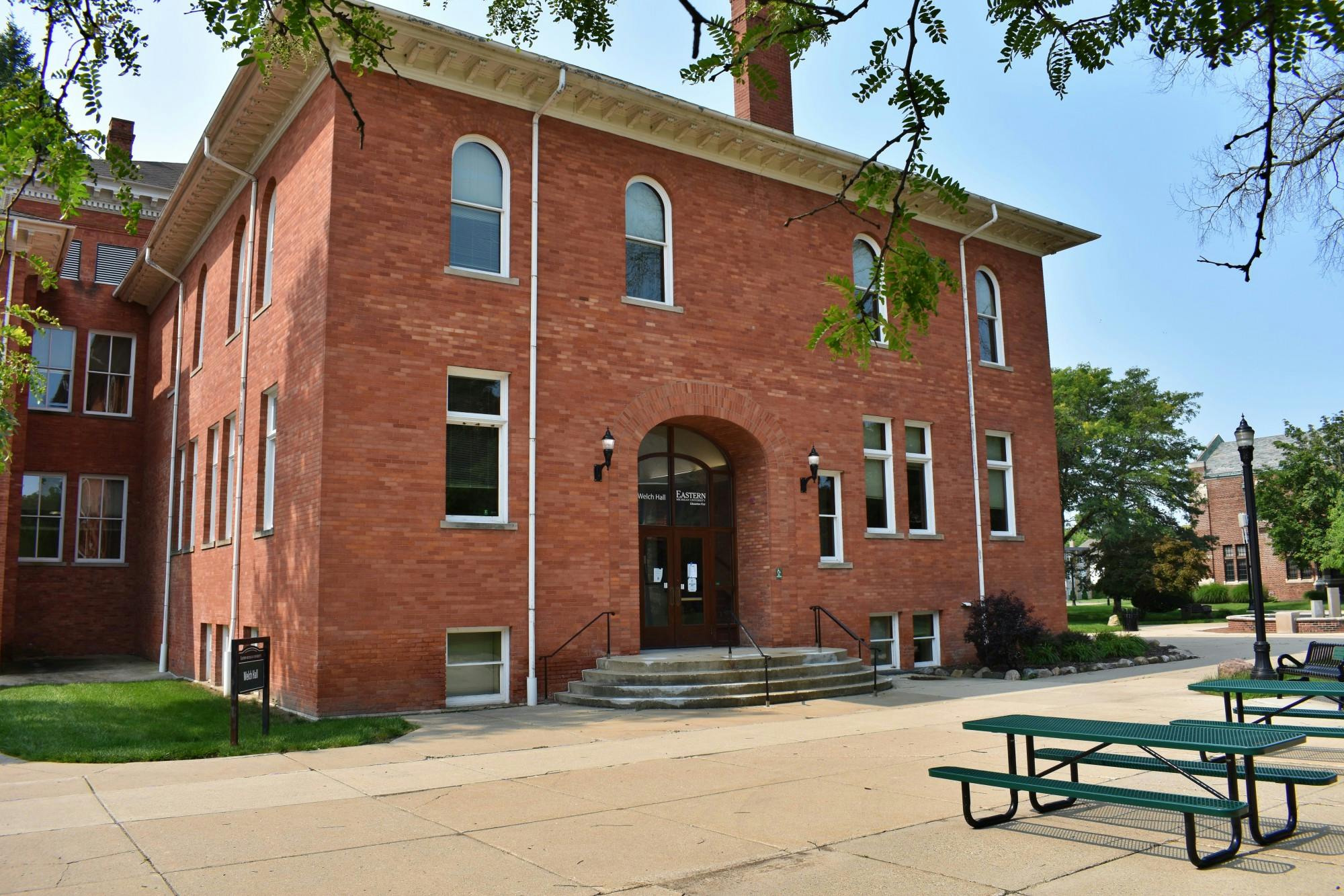A photo of a red brick building with green picnic tables out front.
