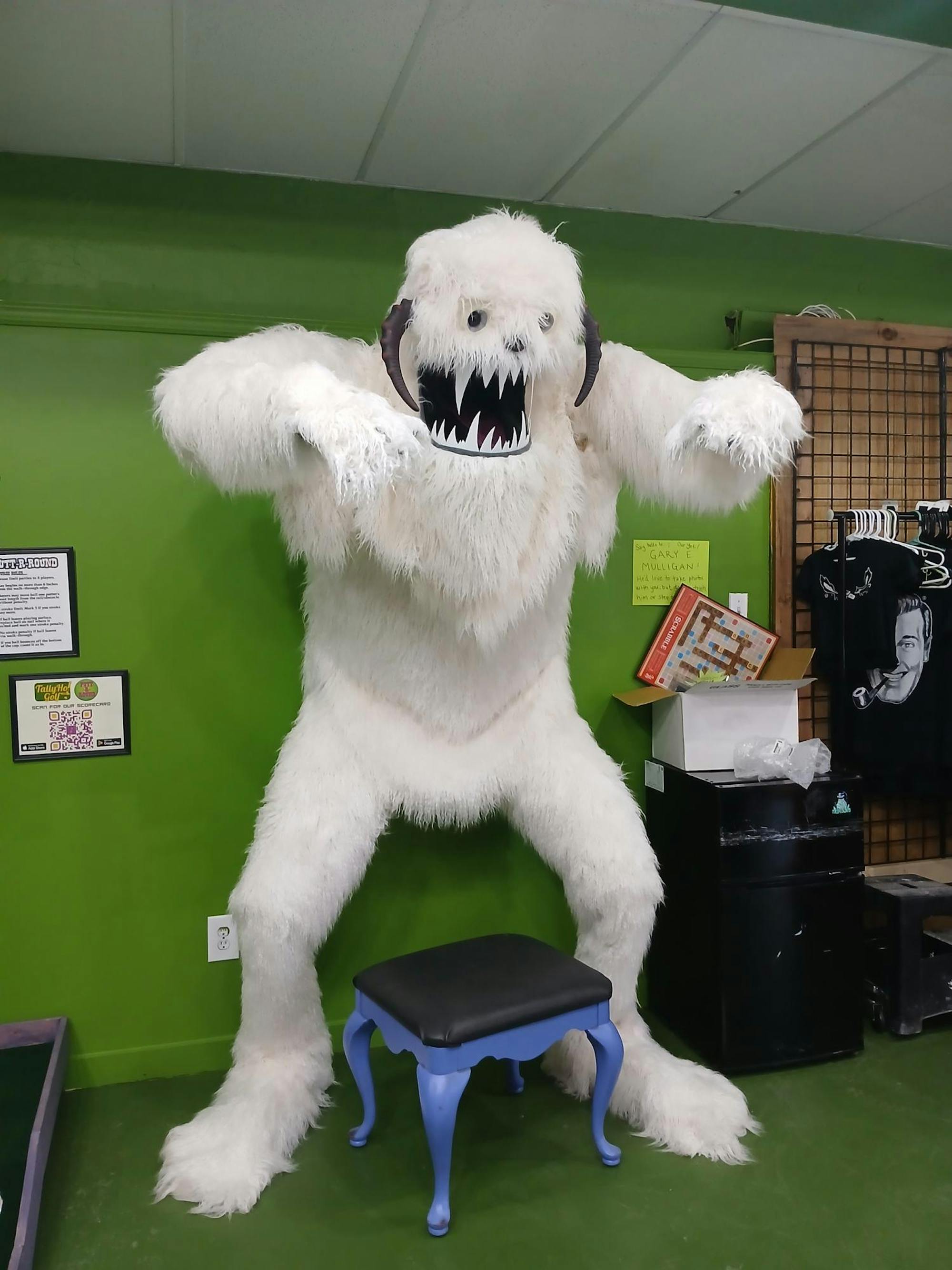 A white furry monster decoration with large fangs stands in front of a green background.