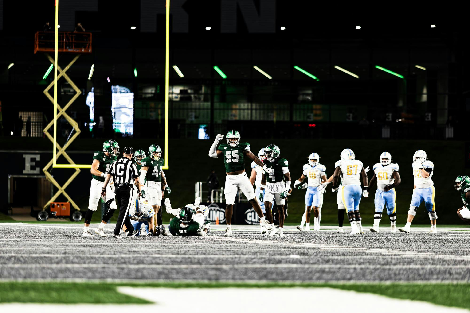 An Eastern Michigan defensive lineman donned in green and white jumps in the air with a fist raised above his head following a defensive stop. 