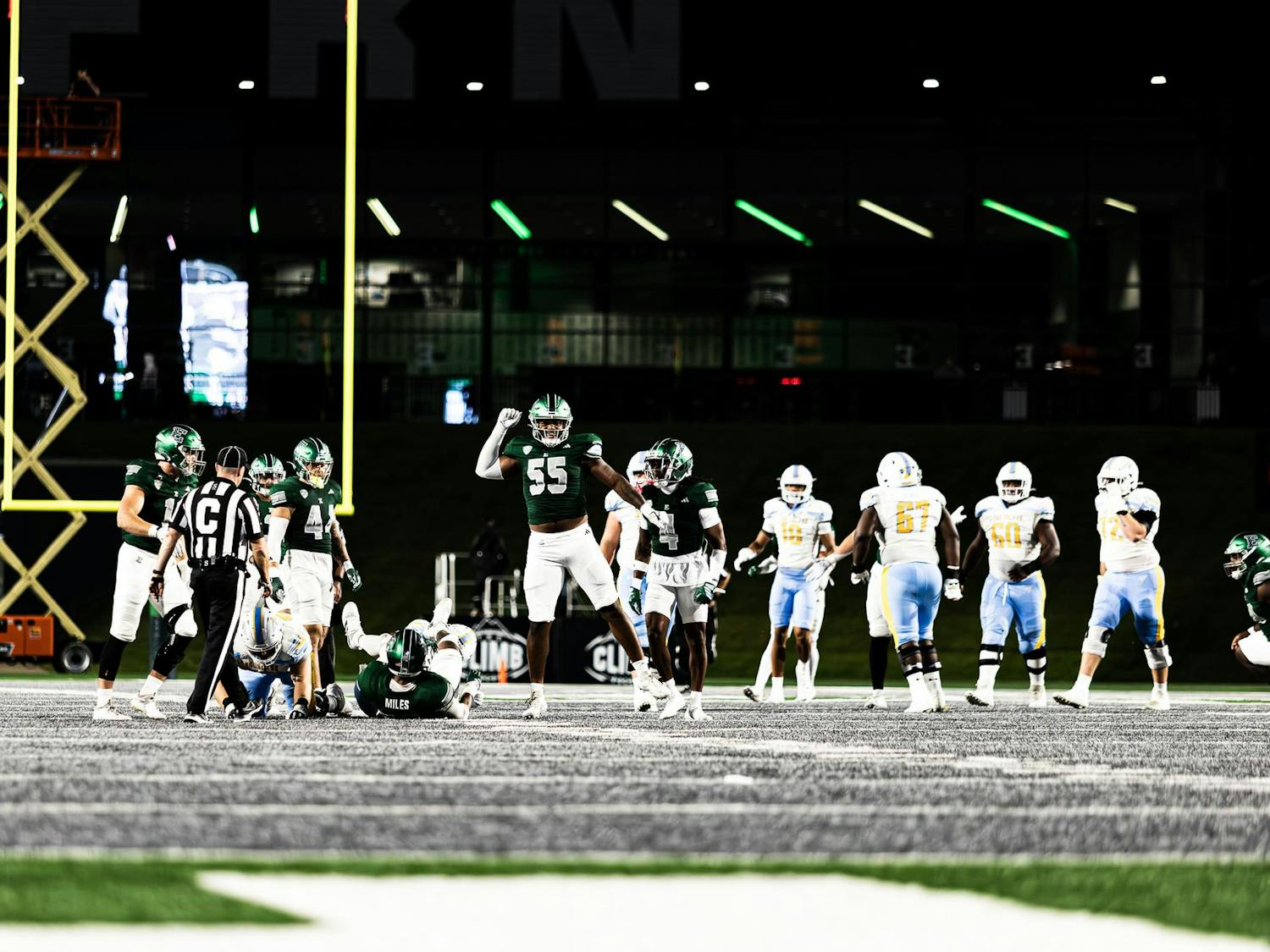 An Eastern Michigan defensive lineman donned in green and white jumps in the air with a fist raised above his head following a defensive stop.