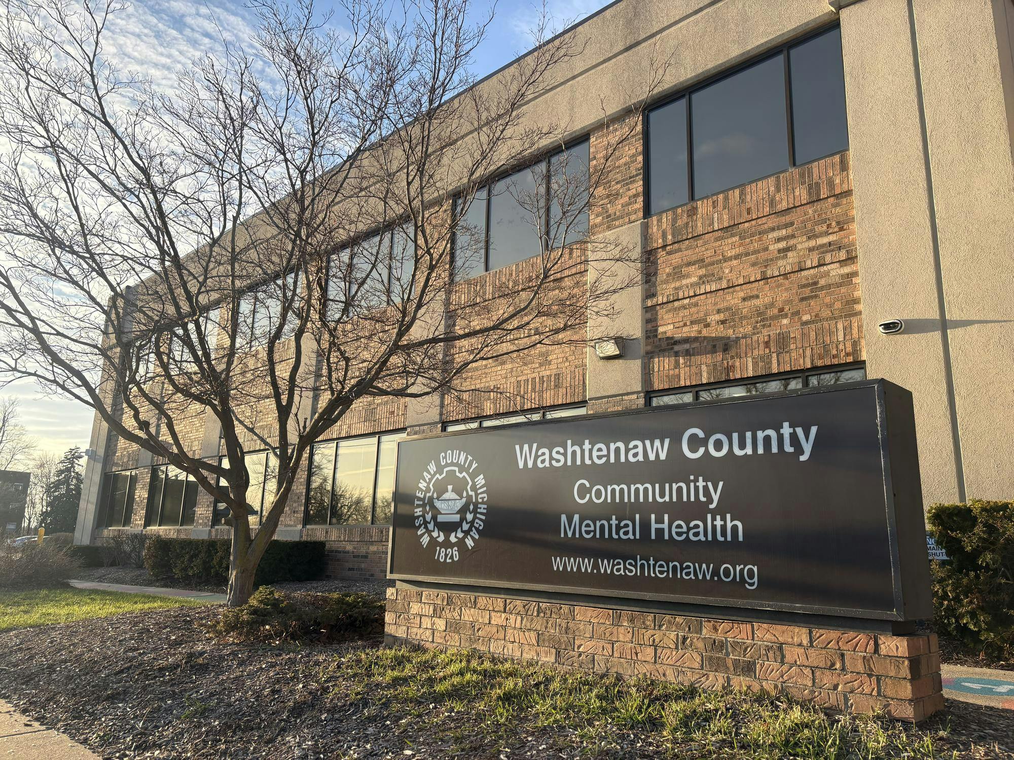 Brown and beige brick and concrete building. A sign in front reads, "Washtenaw County Community Mental Health, www.washtenaw.org."