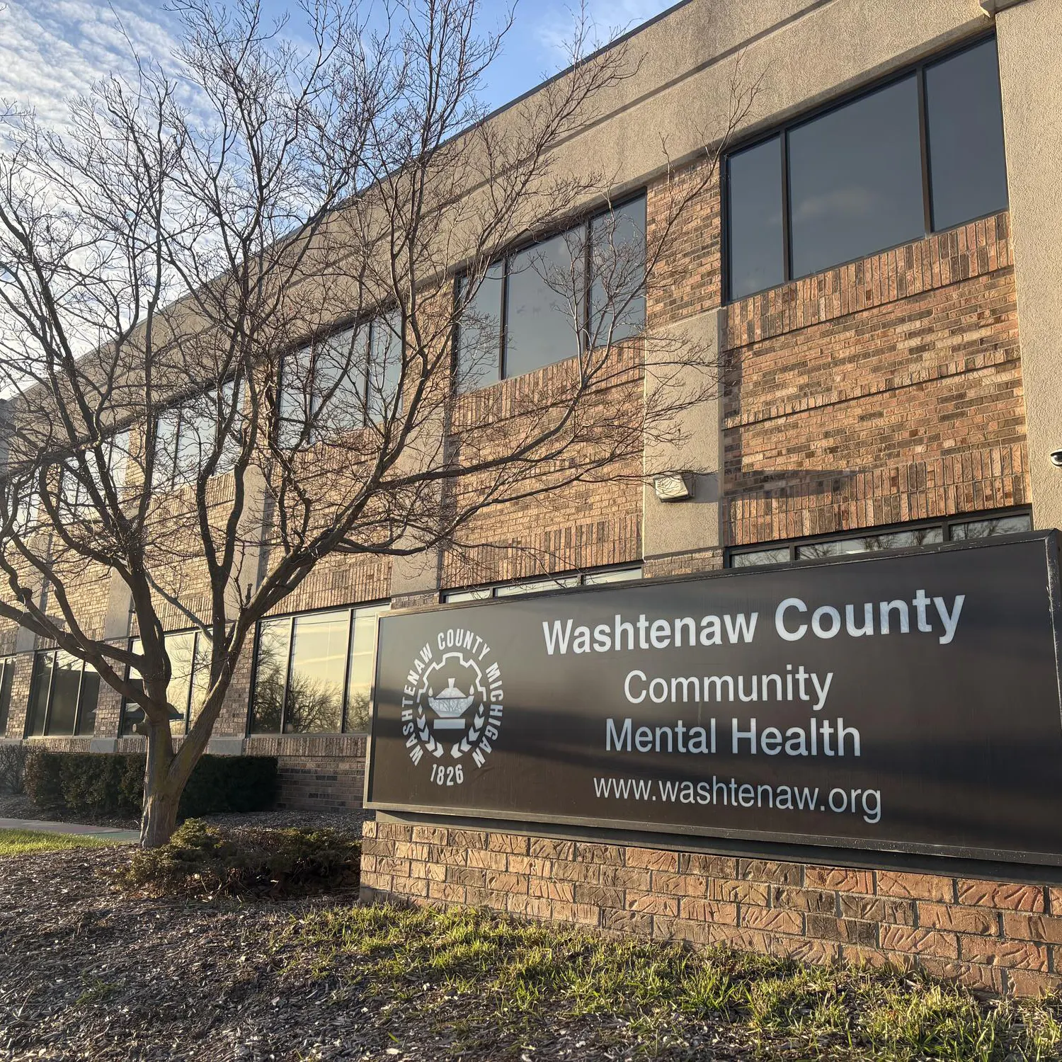 Brown and beige brick and concrete building. A sign in front reads, "Washtenaw County Community Mental Health, www.washtenaw.org."