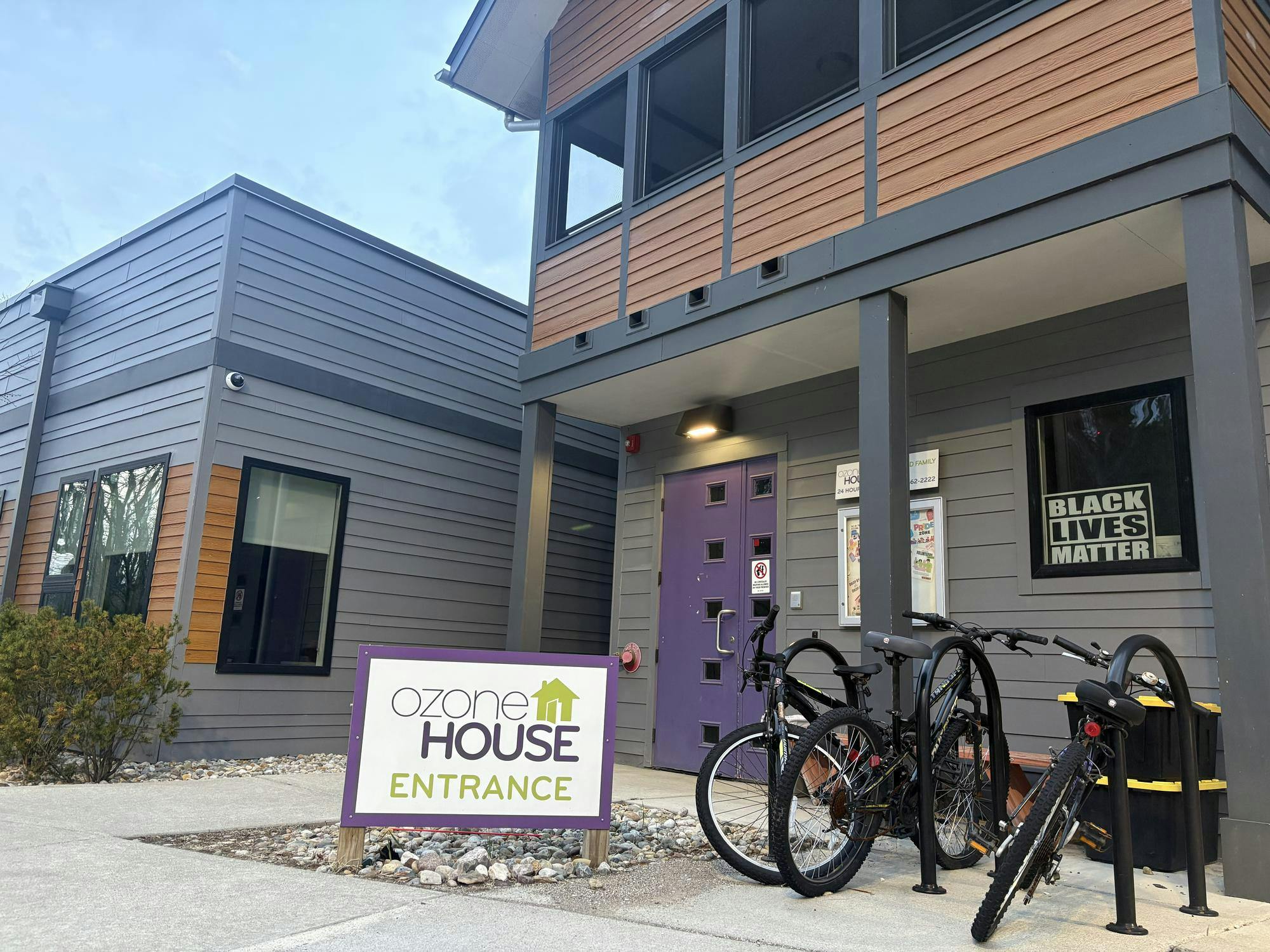 Modern-style gray and brown Ozone House building. A sign in front reads, "Ozone House Entrance."