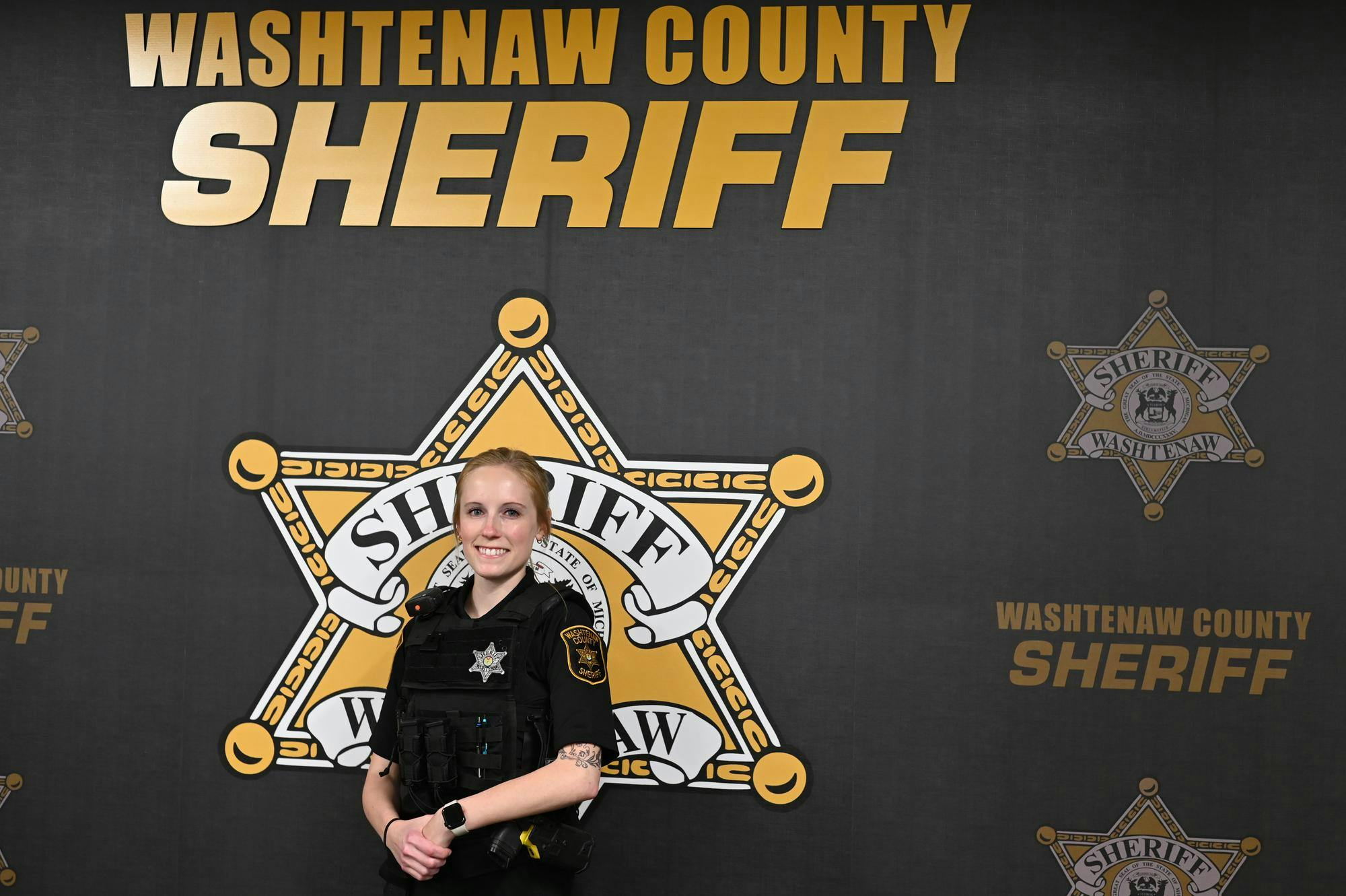 Jessica VanBynen stands in uniform in front of a backdrop with the Washtenaw County Sheriff's Office logo.
