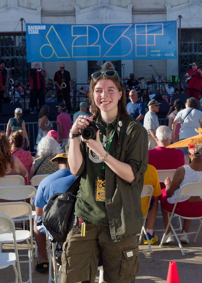 Max Taylor stands at an outdoor event, smiling and holding a camera.
