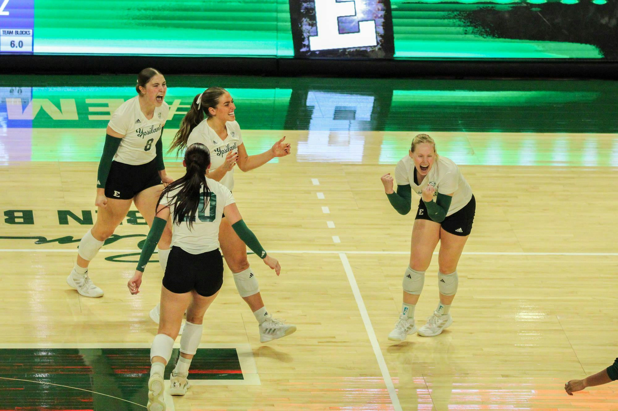 EMU Women's Volleyball players all cheering after getting a point, all in white jerseys. 