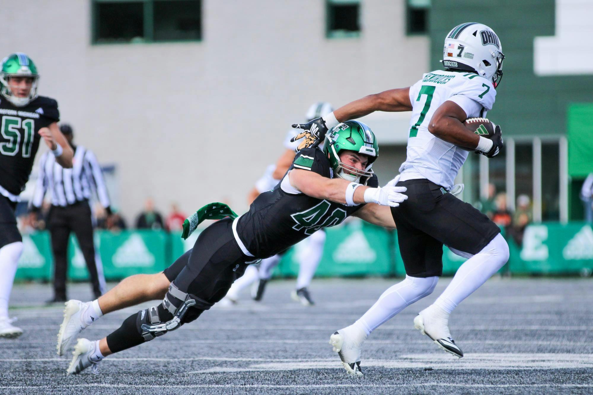 EMU's football player, in a black jersey, tackles Ohio's player, in a white jersey.