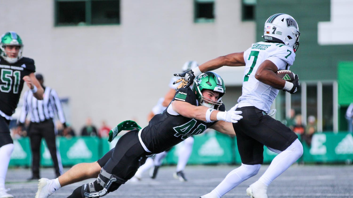 EMU's football player, in a black jersey, tackles Ohio's player, in a white jersey.