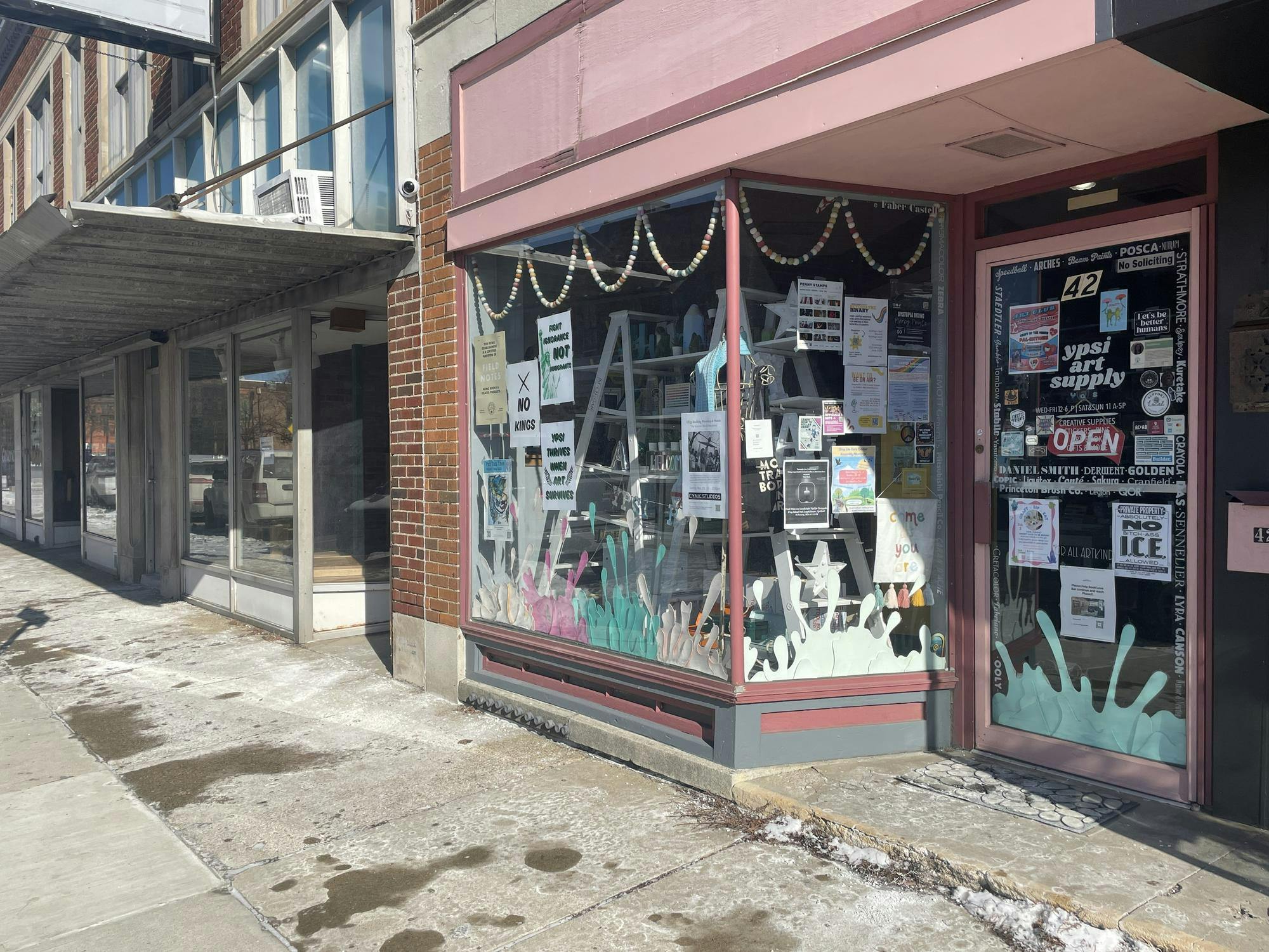Store windows for a brick building with pink trim. The inside of the windows are covered in posters and decorations.