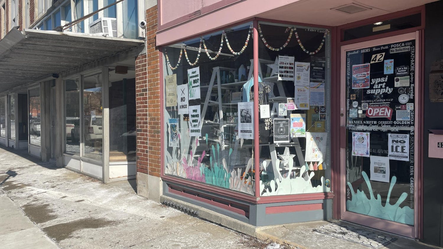 Store windows for a brick building with pink trim. The inside of the windows are covered in posters and decorations.