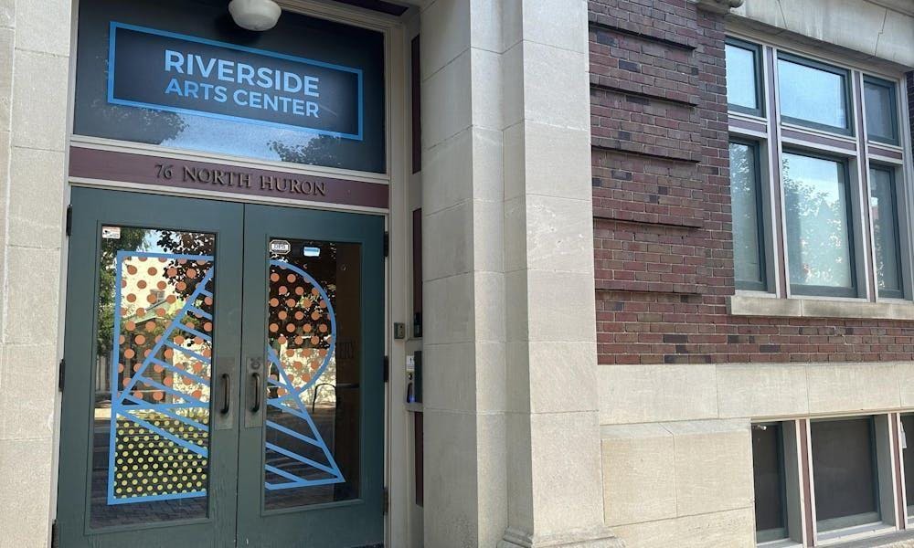 Doorway to a gray cement and red brick historic building. The glass double-door entrance has the letter "R" painted on the front in colorful patterns.